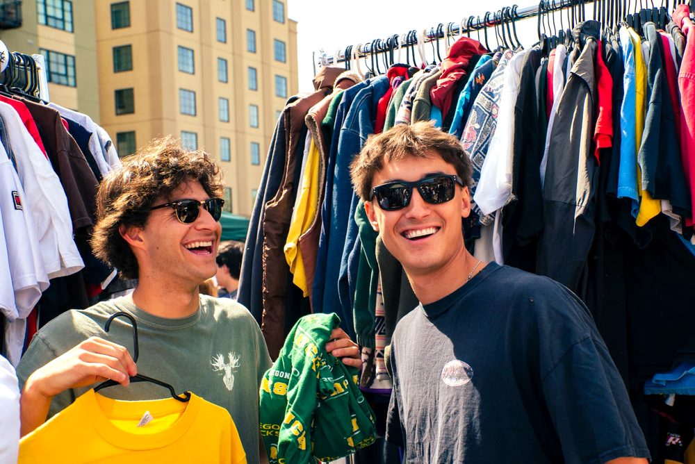 Two friends holding up the shirts they picked out and laughing at the racks